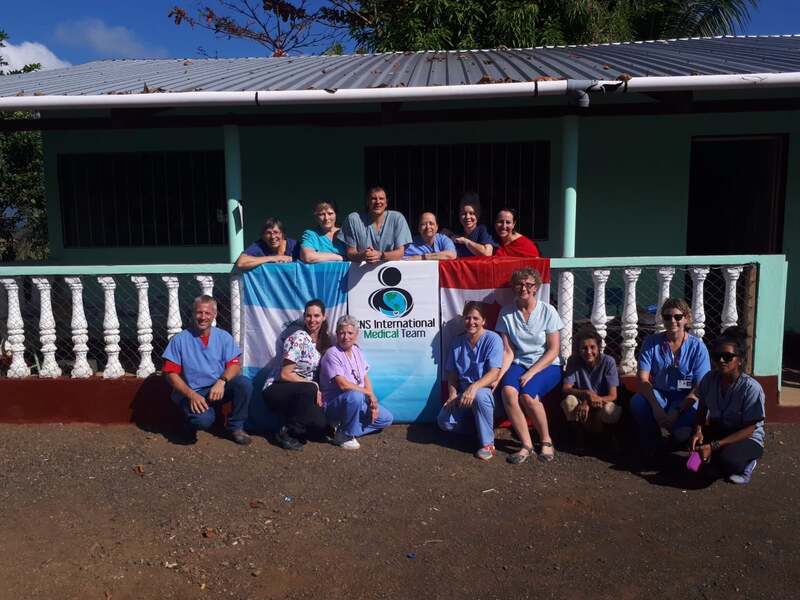 A volunteer group photo in front of the clinic sign.