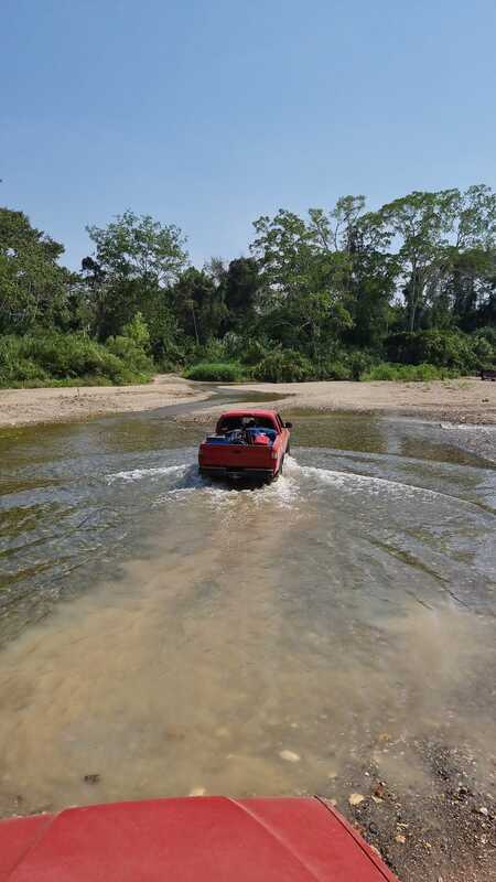 A red pick-up truck driving through a shallow river.