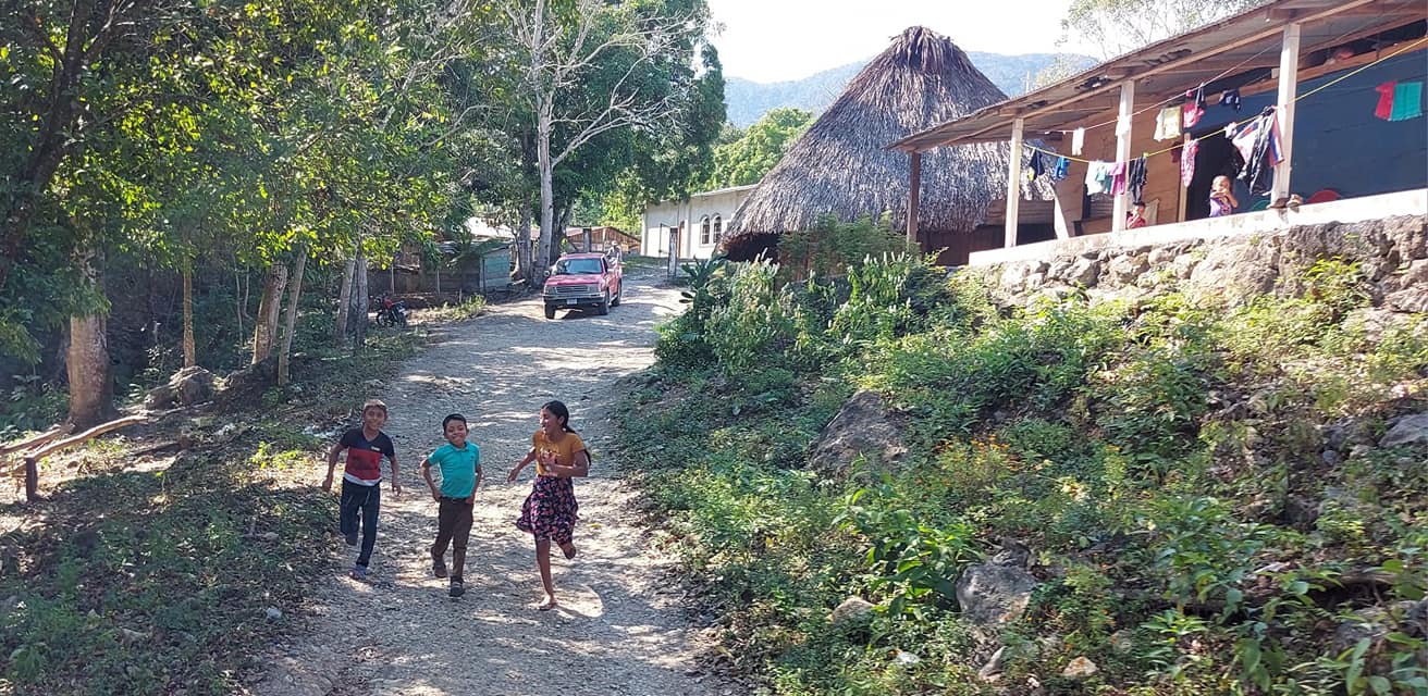Three children running down a road towards the clinic.
